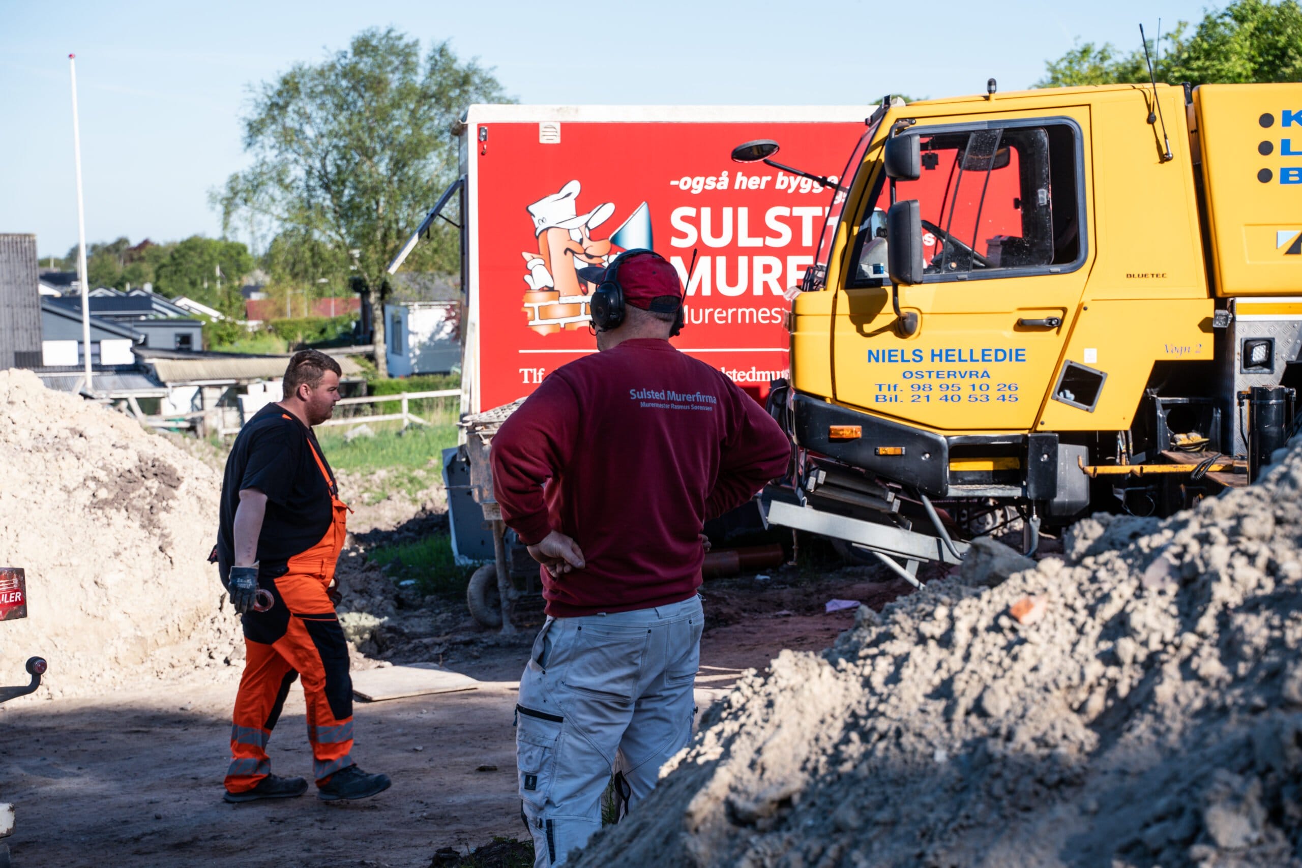 Bygningsarbejdere på byggeplads med lastbiler i baggrunden