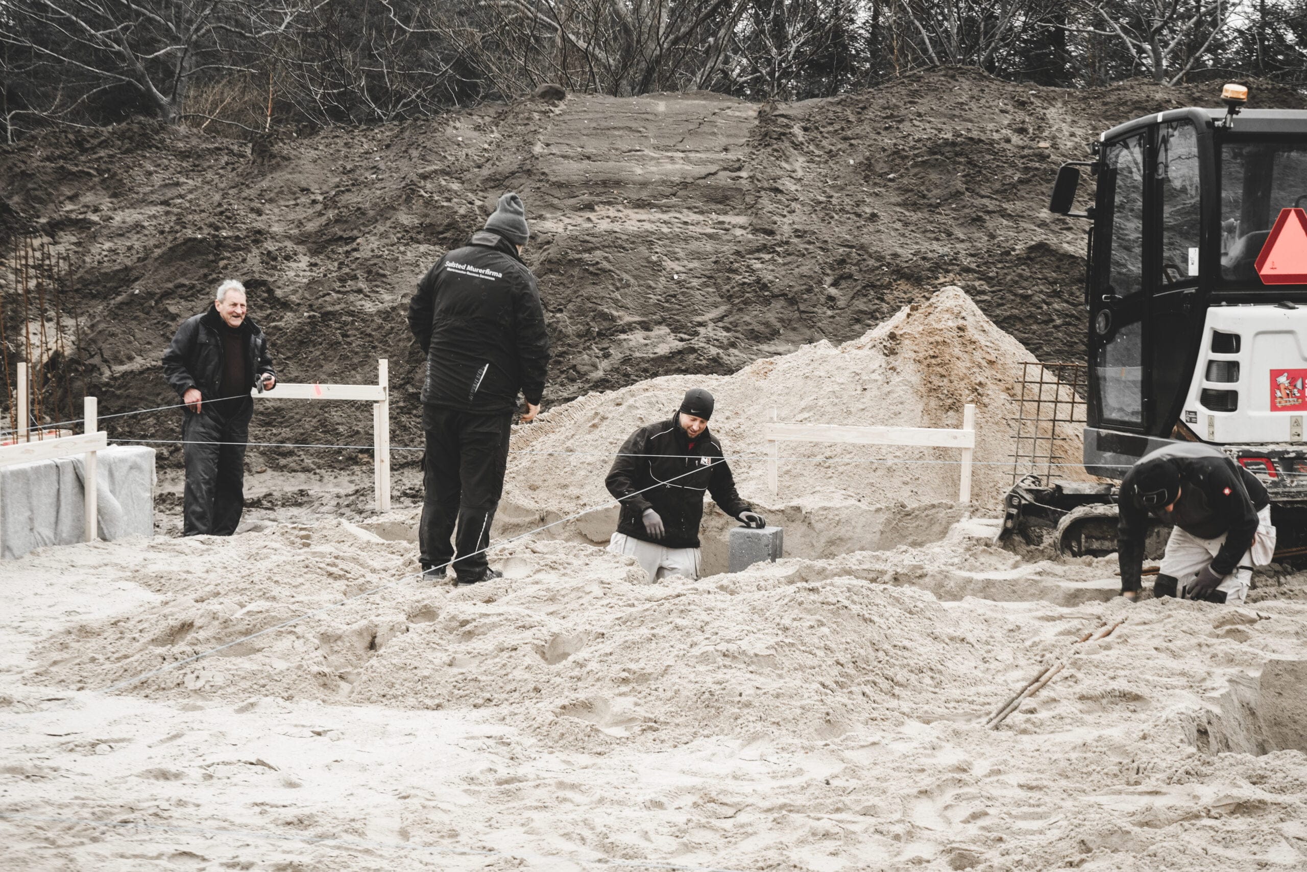 Arbejdere forbereder byggeplads med sand og gravemaskine