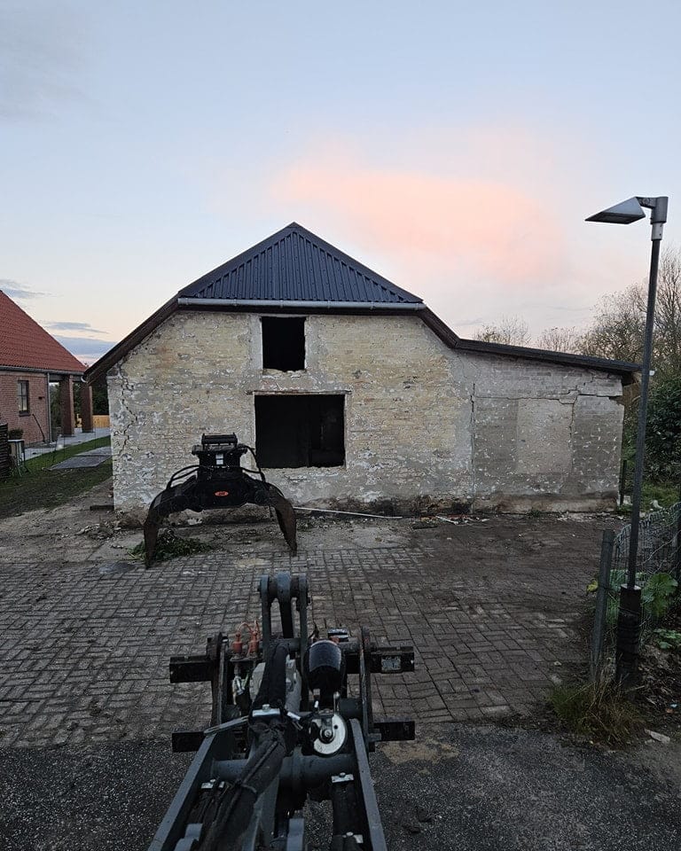 Nedrevet bygning med gravemaskine foran ved solnedgang