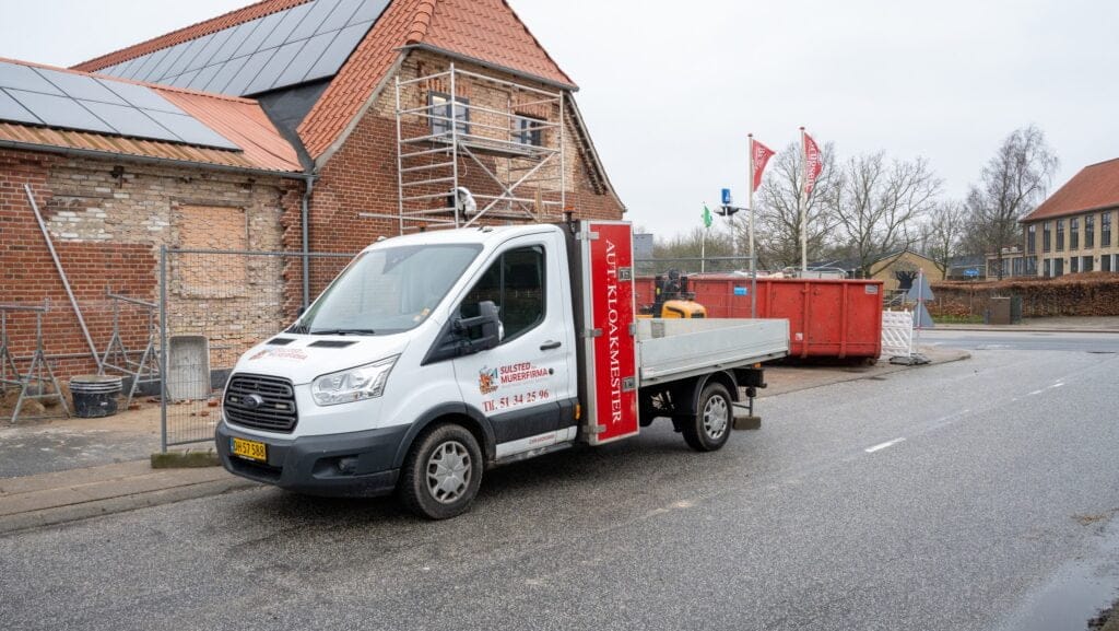 Murervirksomhedens varevogn ved byggeplads med murstenshus