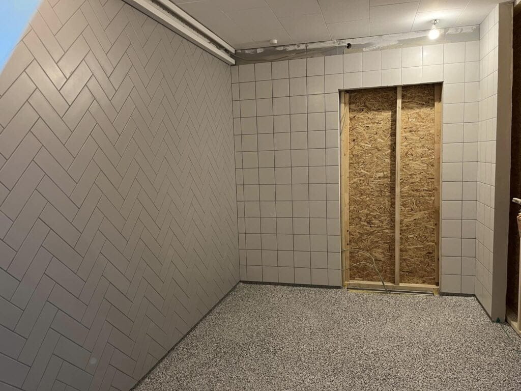 Ufærdigt rum med flisebelagte vægge og spånpladeåbning